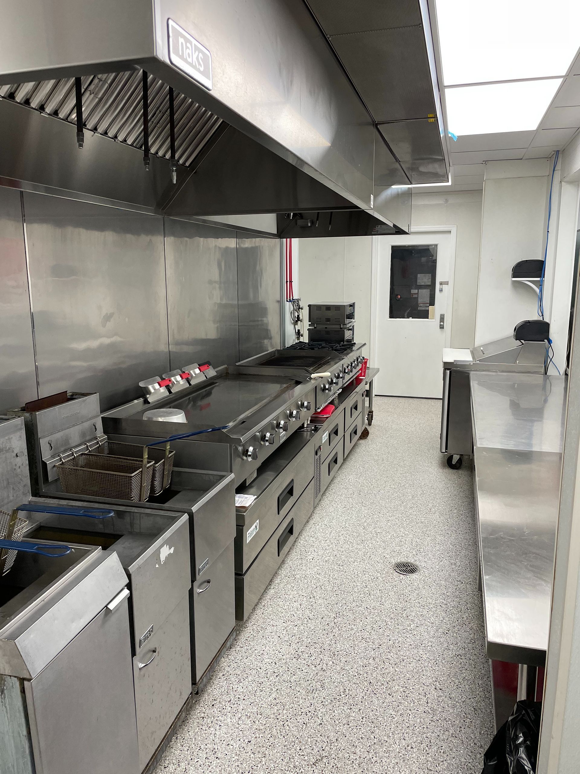 Commercial kitchen with stainless steel appliances, vent hood, and a narrow layout.