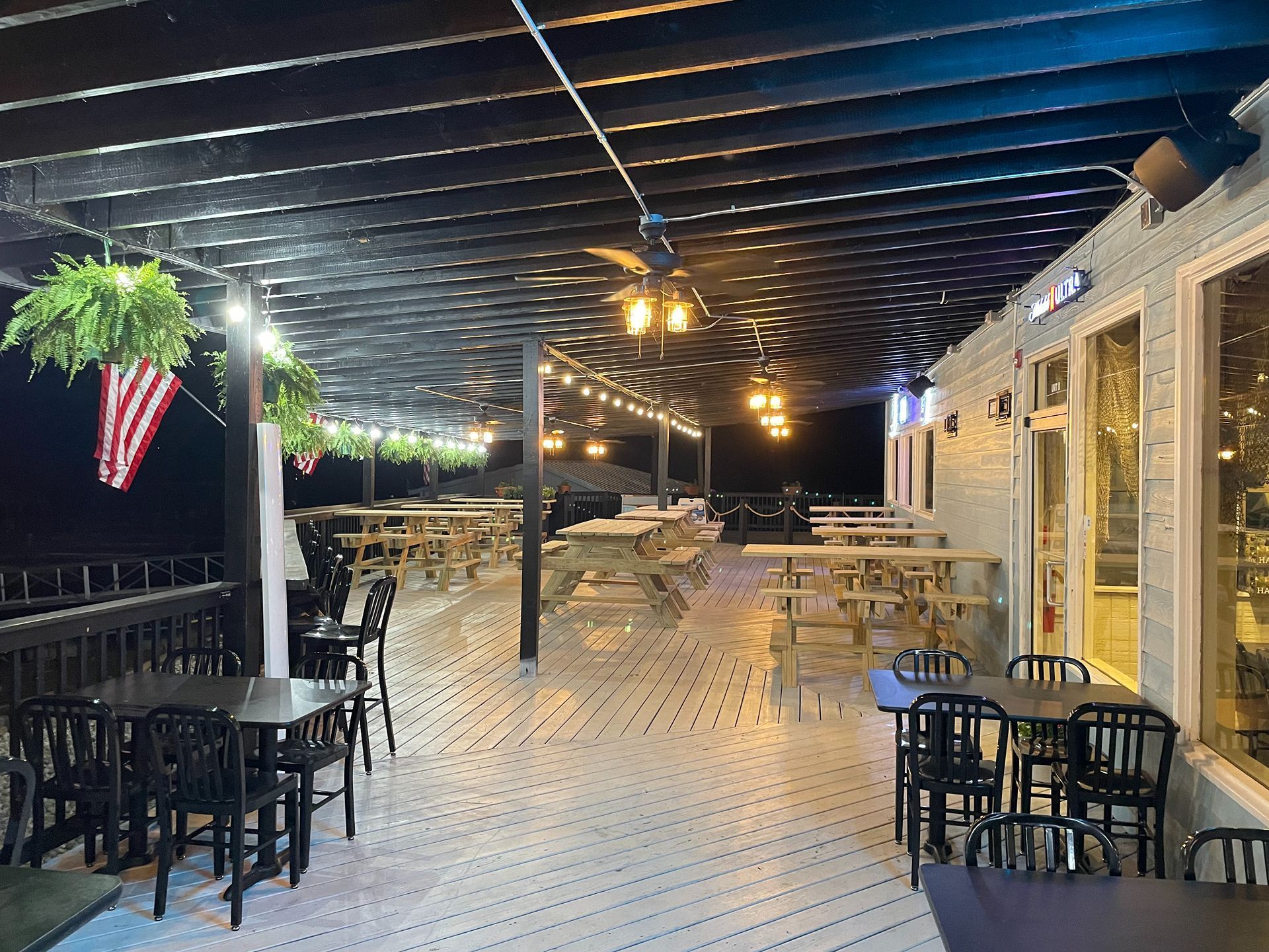 Outdoor restaurant patio at night with tables, chairs, string lights, and a view.