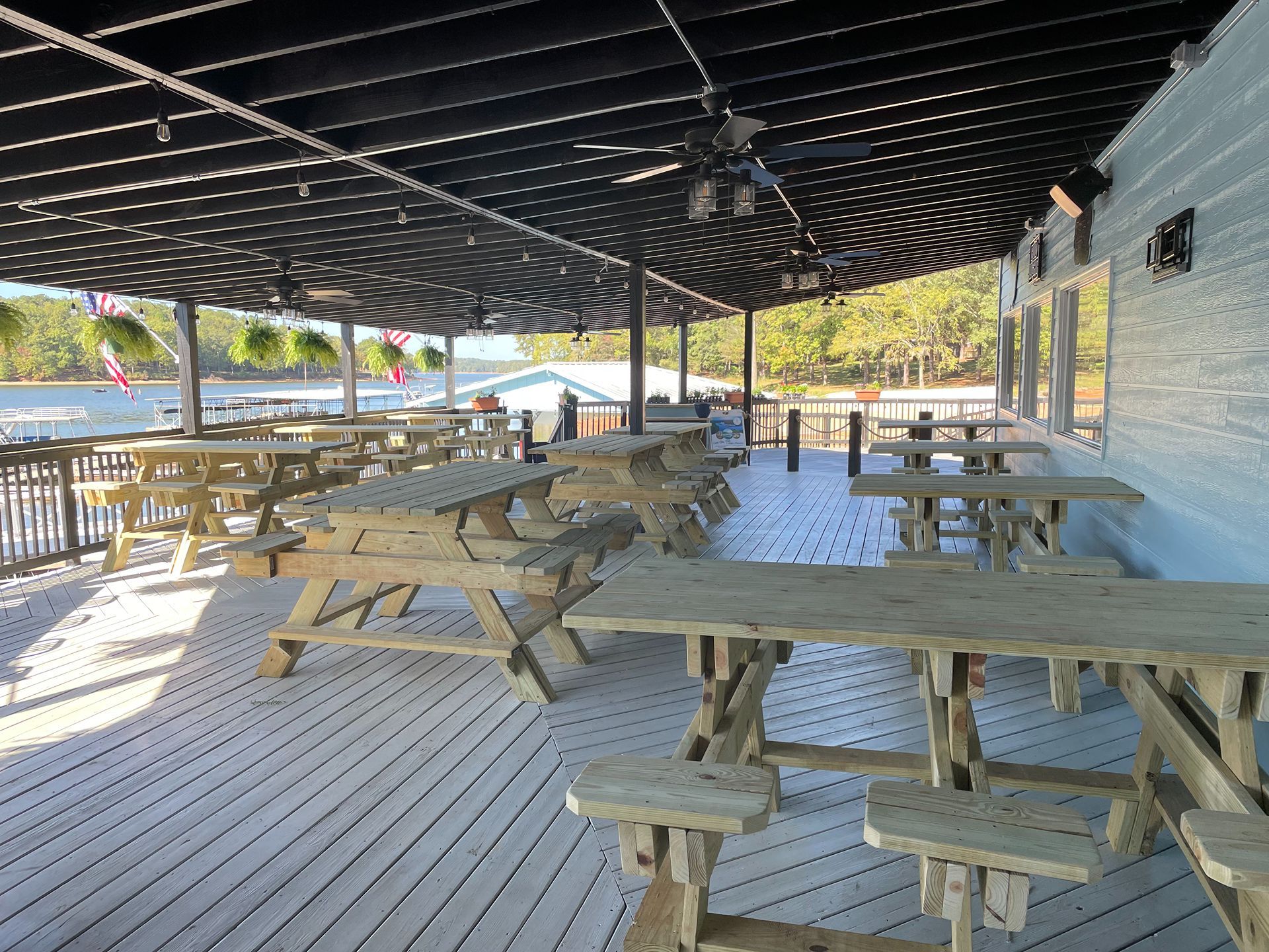 Outdoor restaurant patio with picnic tables under a dark latticed roof, overlooking a body of water.