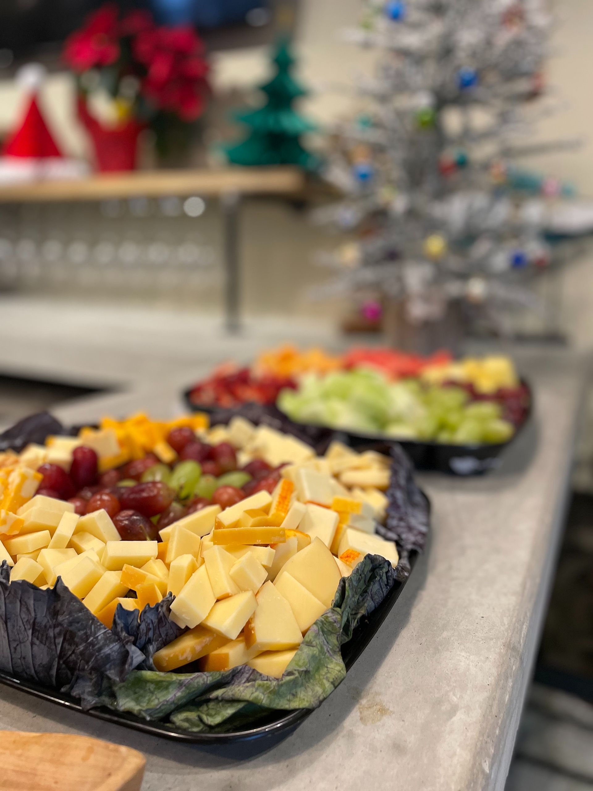 Cheese and fruit platters on a counter with Christmas decorations blurred in the background.