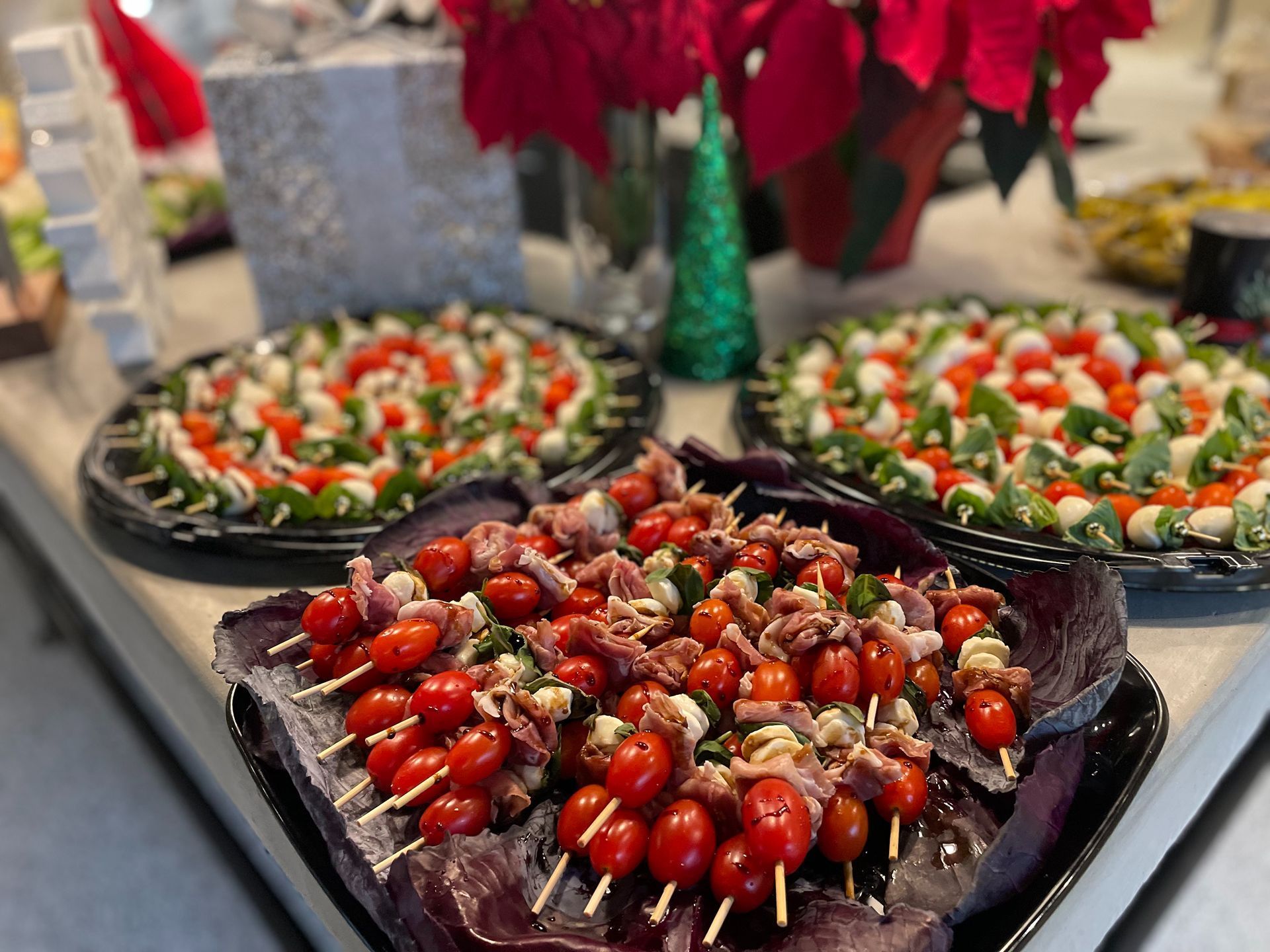 Appetizer skewers with tomatoes, mozzarella, and prosciutto on platters; festive setting with poinsettias.