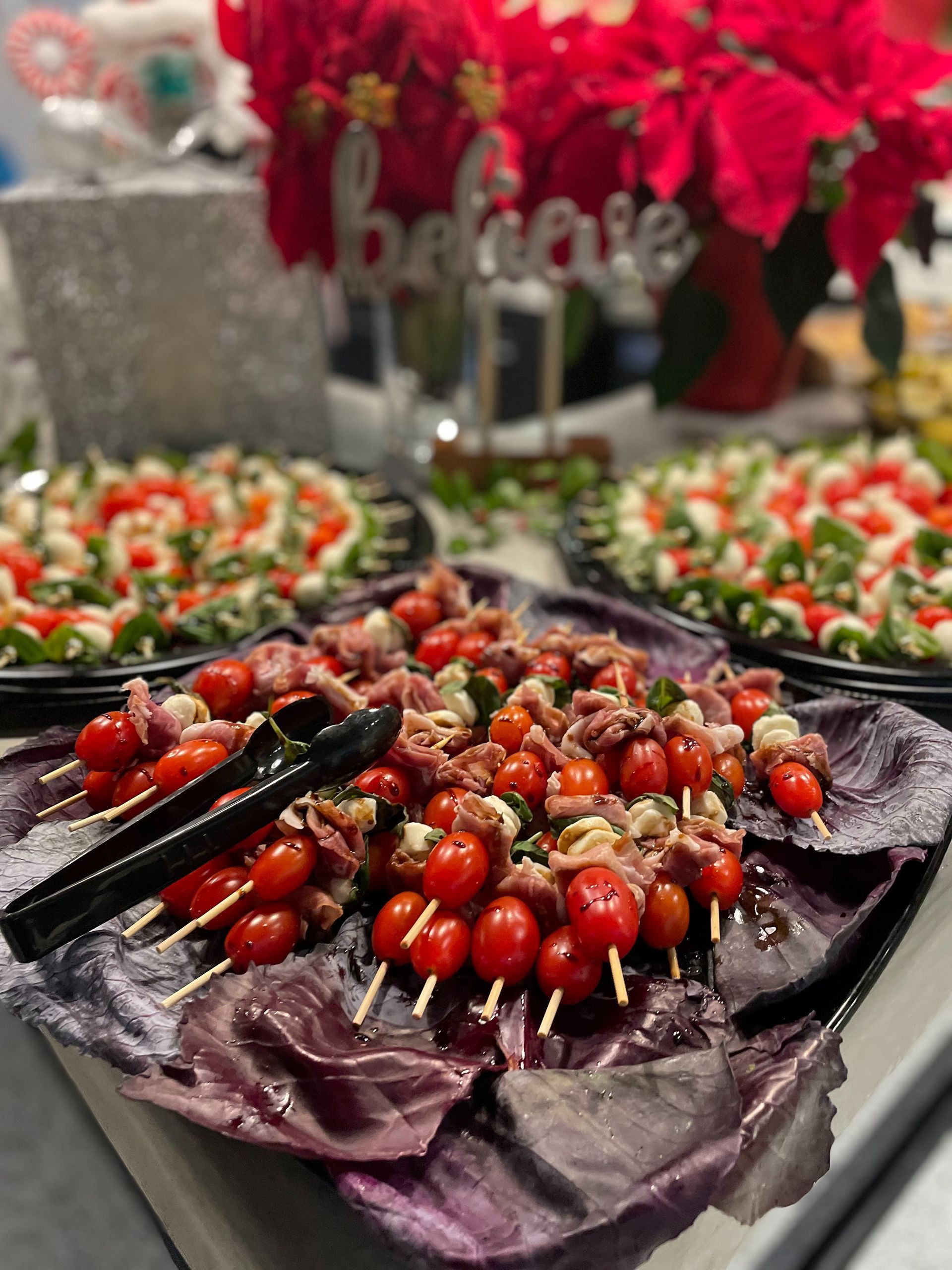 Skewered tomato and mozzarella appetizers on a purple tray with other food platters in the background. 