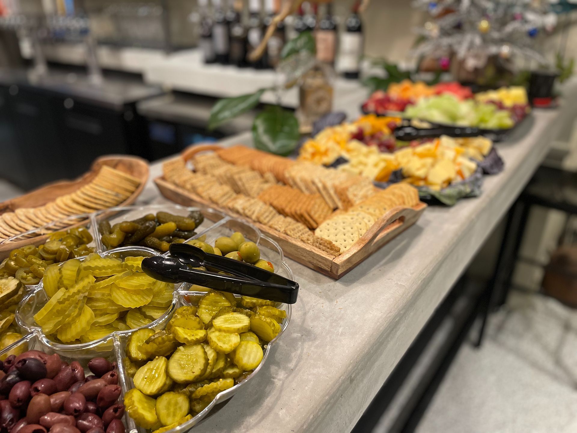 A buffet table with various foods: crackers, cheese, fruit, pickles, and olives.