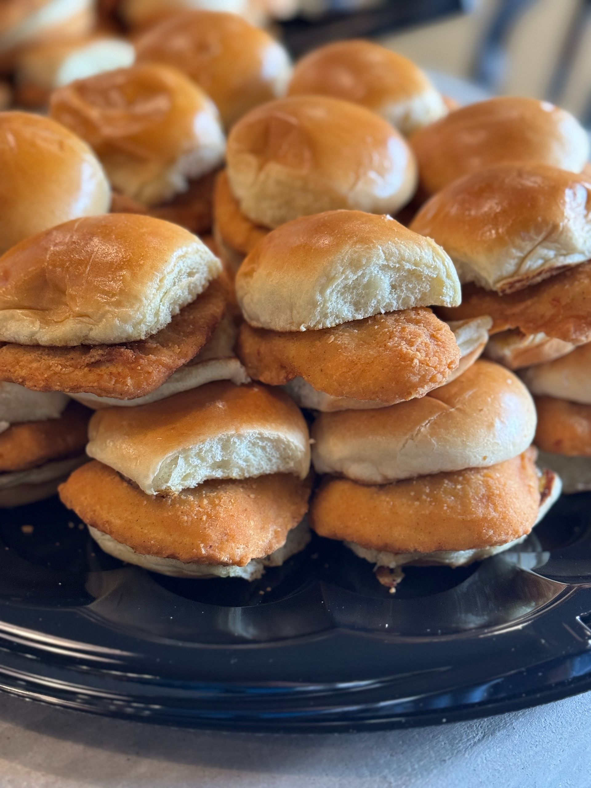 Chicken sliders on a black platter, stacked with golden-brown fried chicken and soft buns.