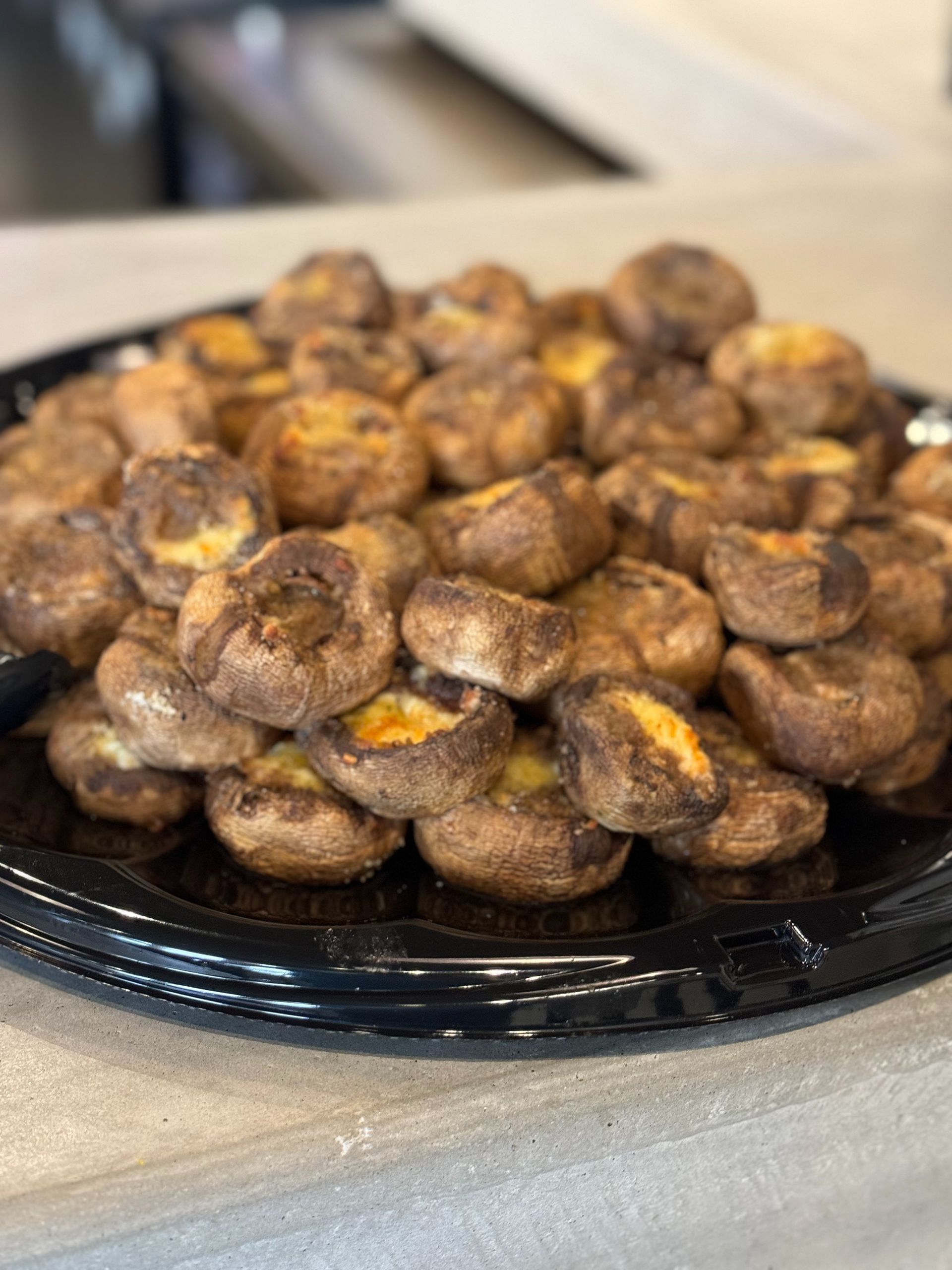 Tray of stuffed mushrooms, brown and gold, arranged on a black serving platter.