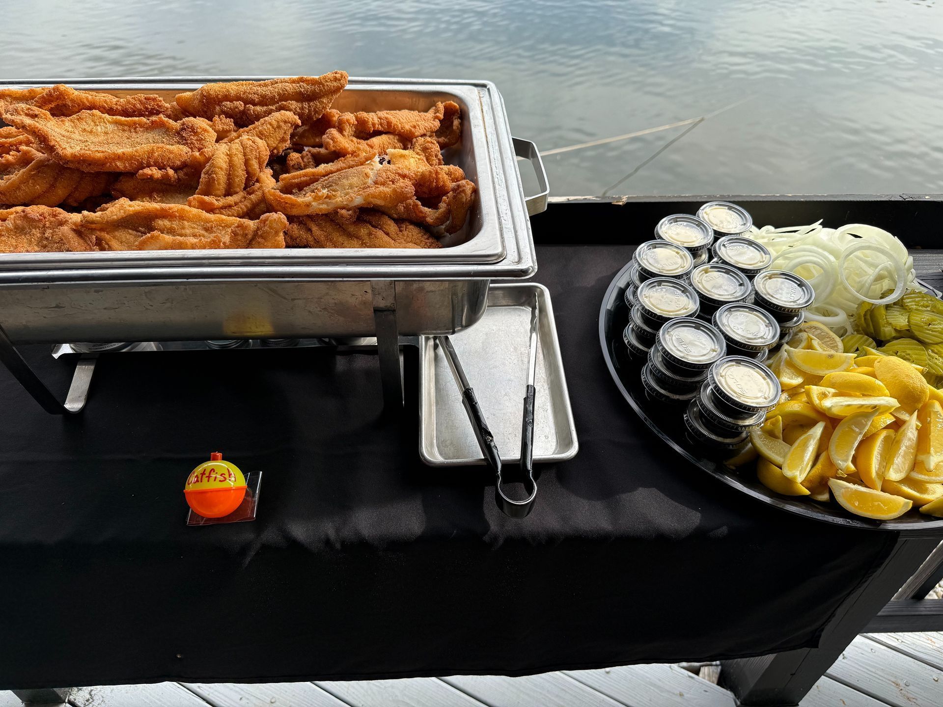 Fried fish buffet with condiments, including lemons, onions, pickles, and dipping sauces.
