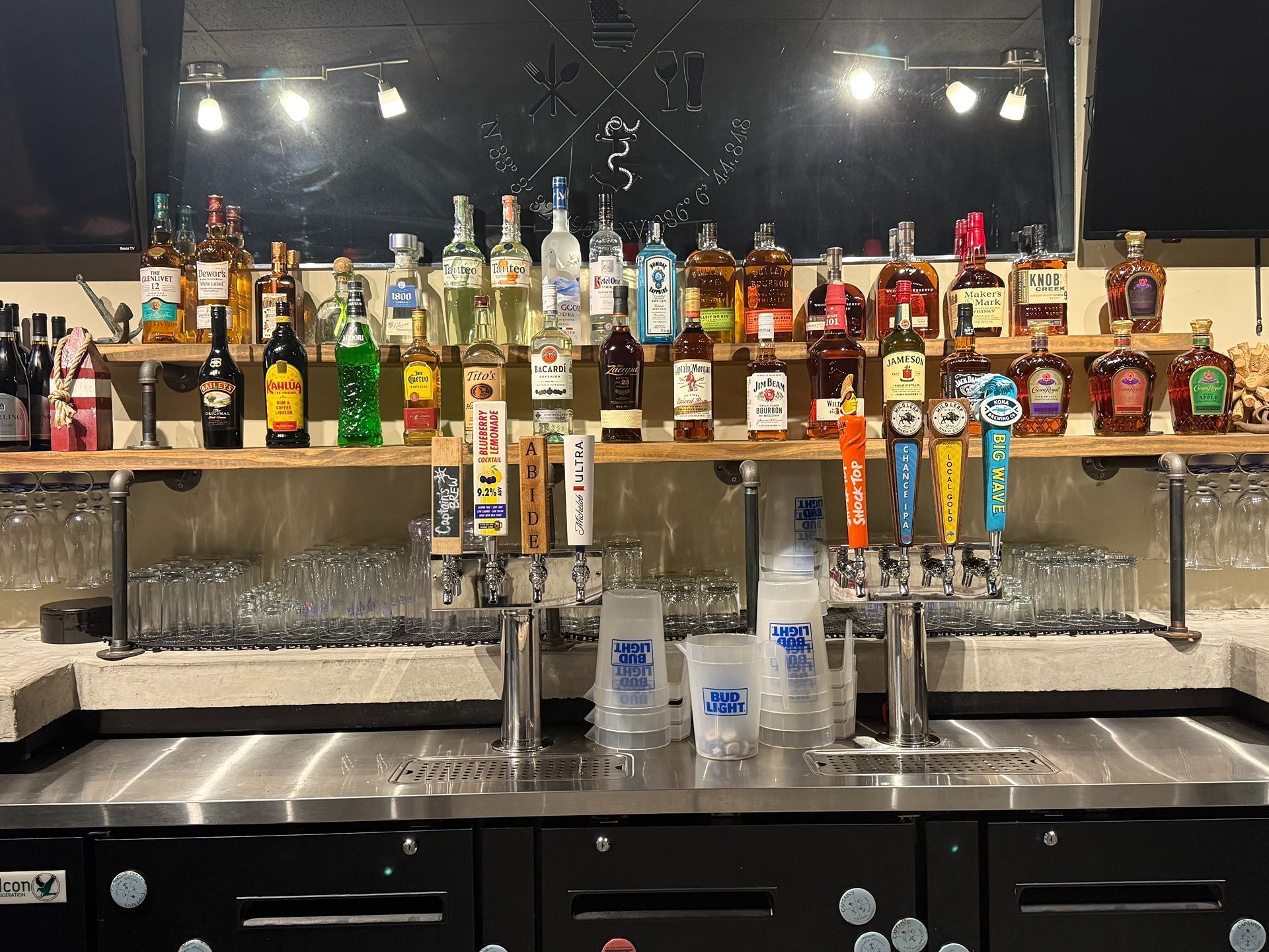 Bar with liquor bottles on shelves, beer taps, and glasses. Stainless steel bar top.
