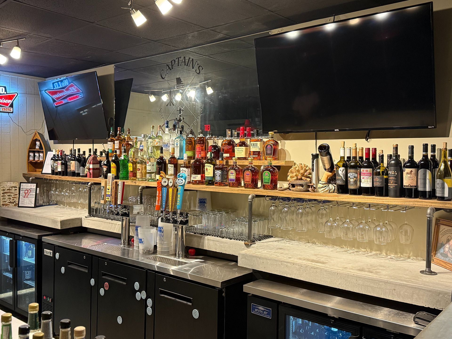 Bar interior with liquor bottles, beer taps, glasses, and two TVs.