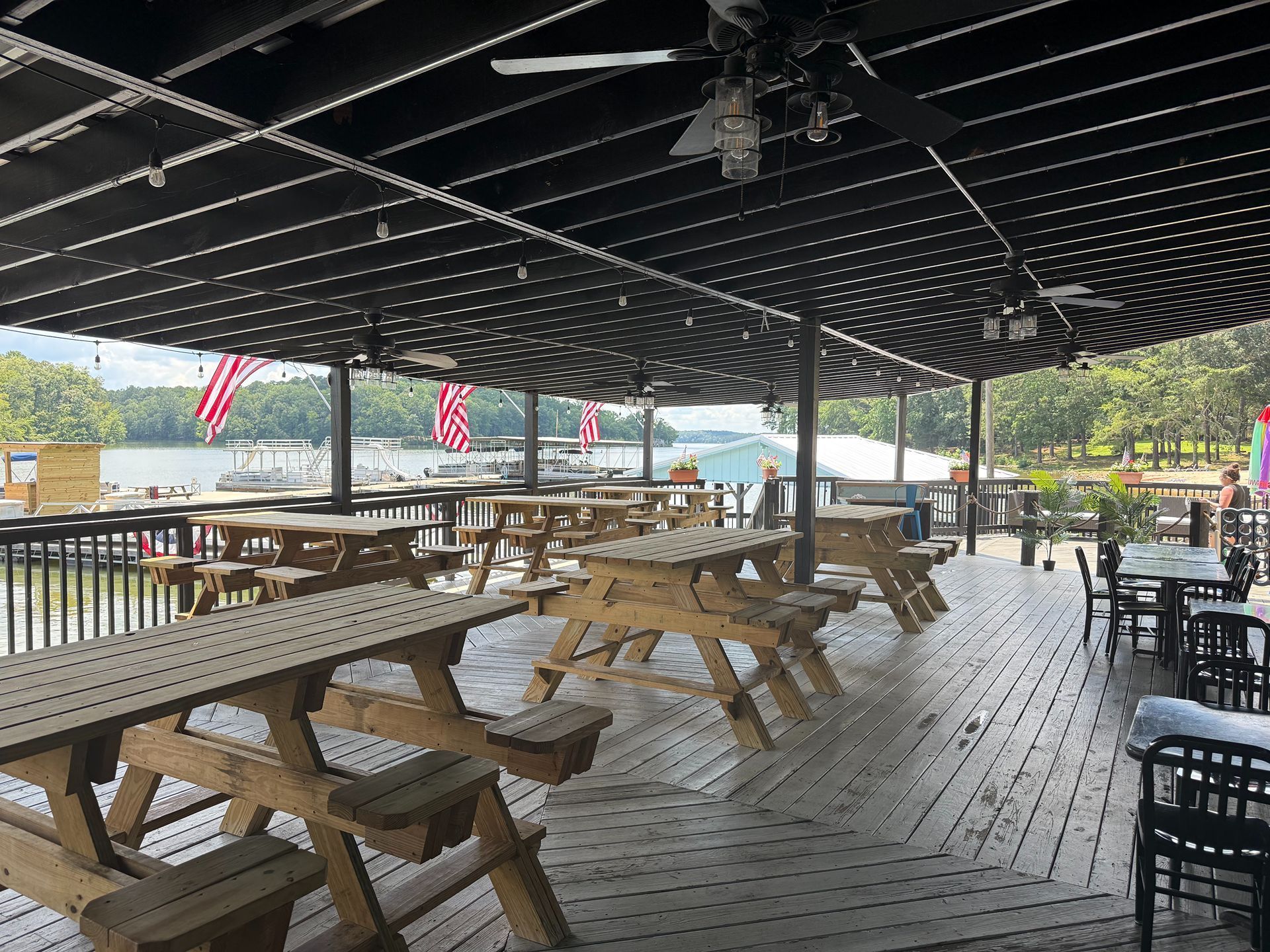 Outdoor deck with picnic tables and lake view under a dark slatted roof.