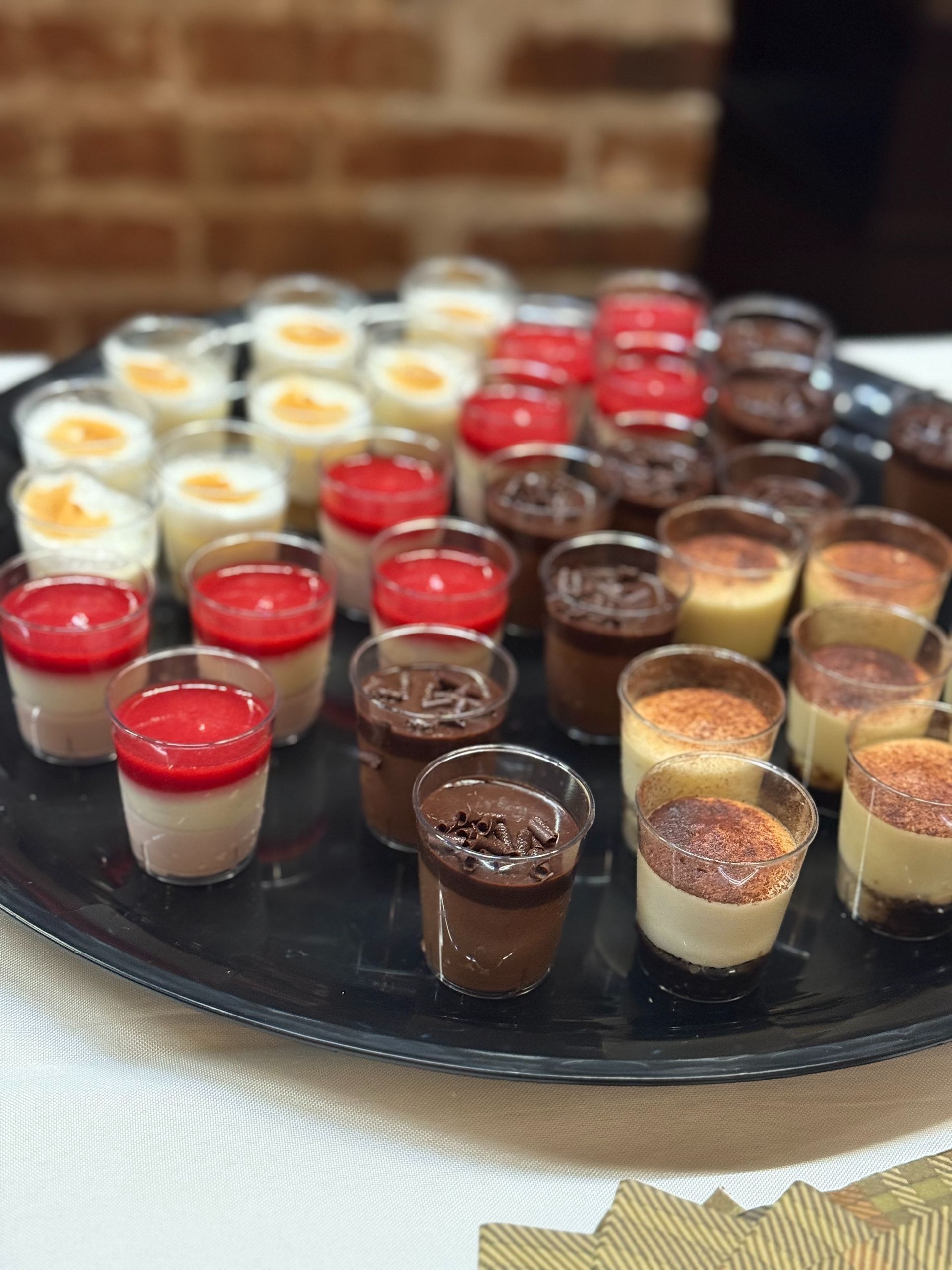 Tray of assorted desserts in clear cups: white, red, chocolate, and caramel.