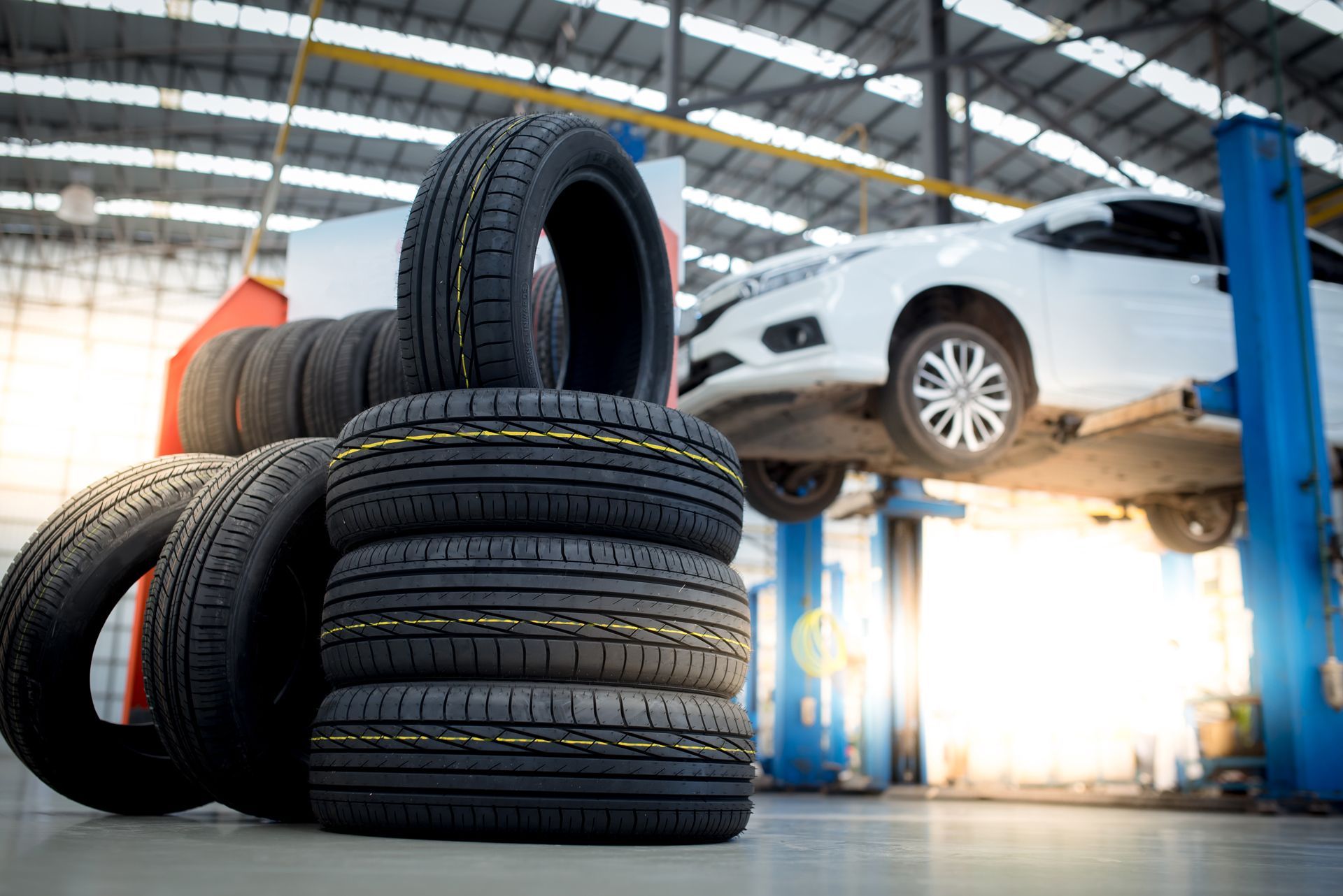 A Stack of Tires in a Garage With a Car in the Background