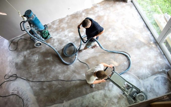 Two men are cleaning a concrete floor with a vacuum cleaner.