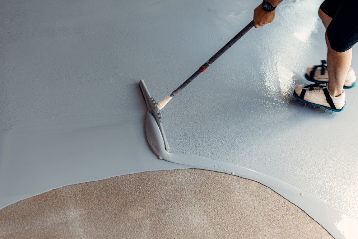 A person is painting a concrete floor with a roller.