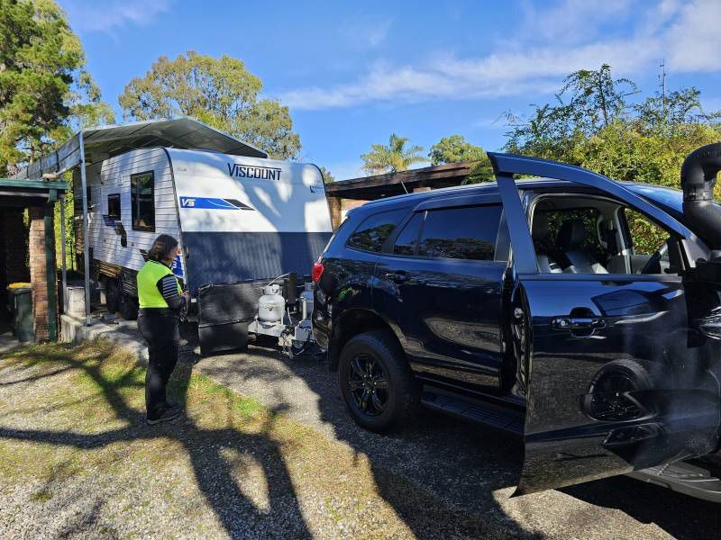 A Man In A Yellow Vest Is Standing In Front Of A Caravan — A Weigh In - Mobile Weighing Solutions in Noraville, NSW