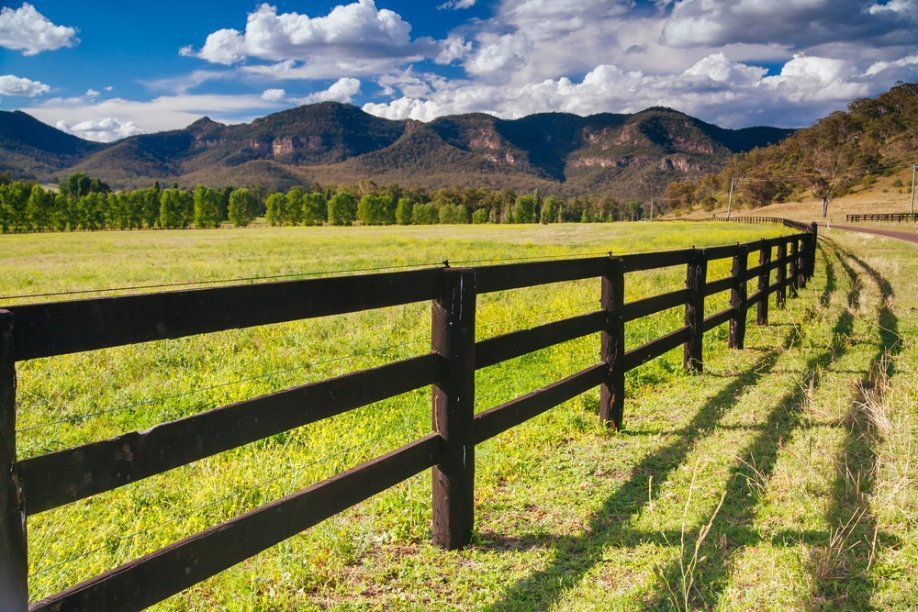 A Wooden Fence Surrounds a Grassy Field with Mountains — A Weigh In - Mobile Weighing Solutions in Muswellbrook, NSW