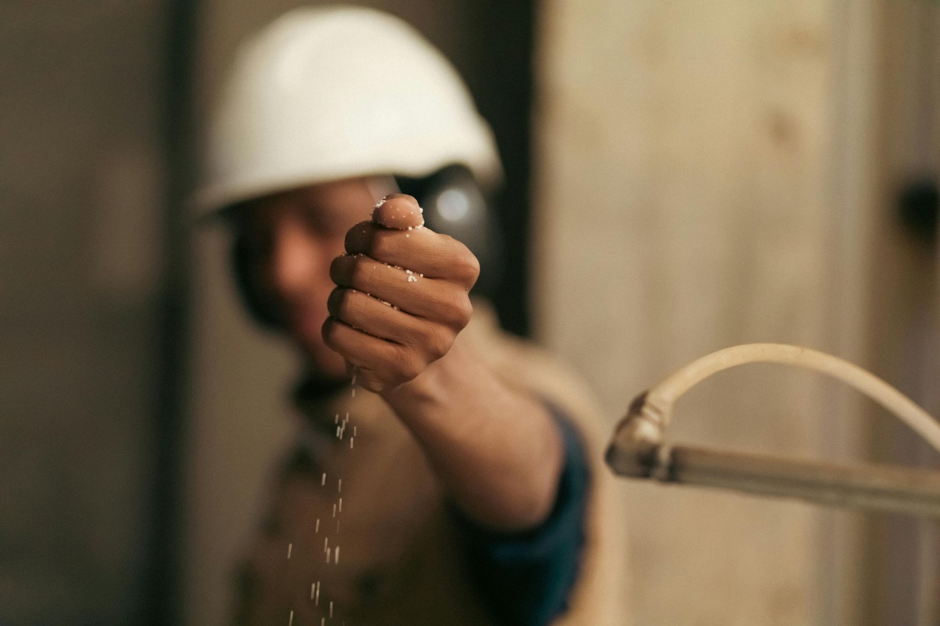 Construction worker in hard hat and ear protection, releasing sawdust in front of wooden structure.