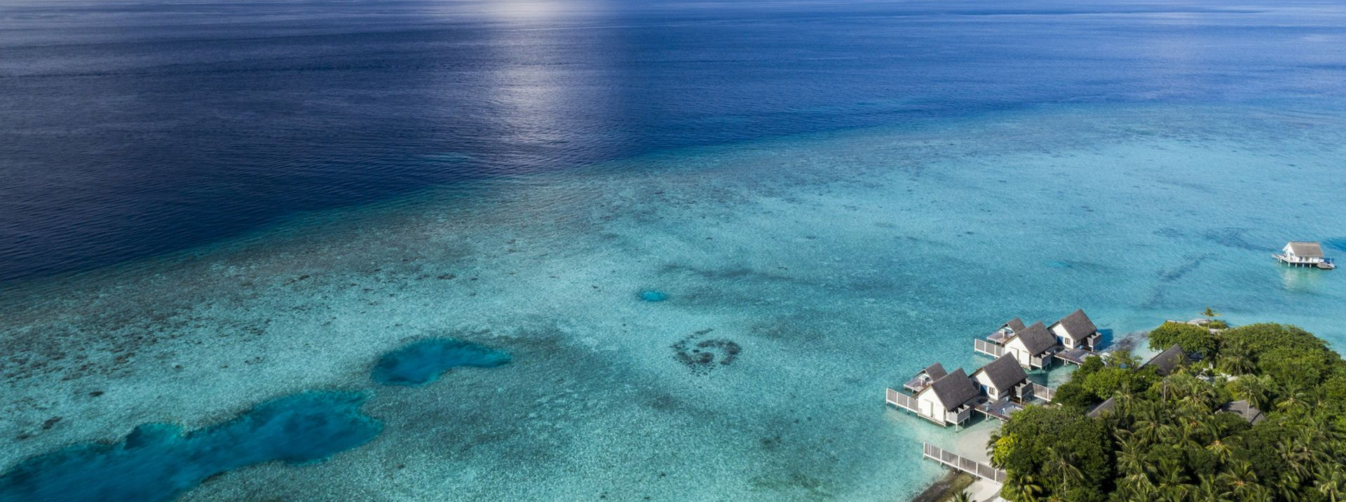 Aerial view of turquoise water with island resort and dark blue ocean.