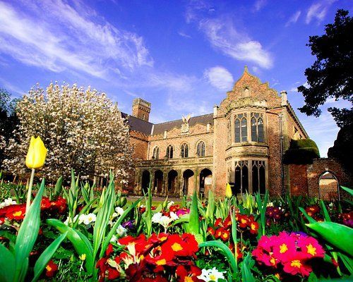 East Midlands. Stone building with arched windows, surrounded by colourful flowers and blossoming trees under a blue sky.