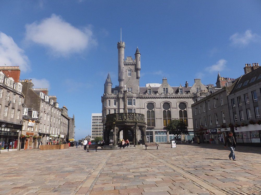 Aberdeen. City square with gray buildings, cobblestones, and a central ornate structure under a blue sky.