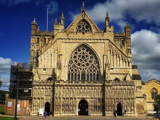 Exeter Cathedral's ornate west front, stone architecture, large rose window, blue sky.