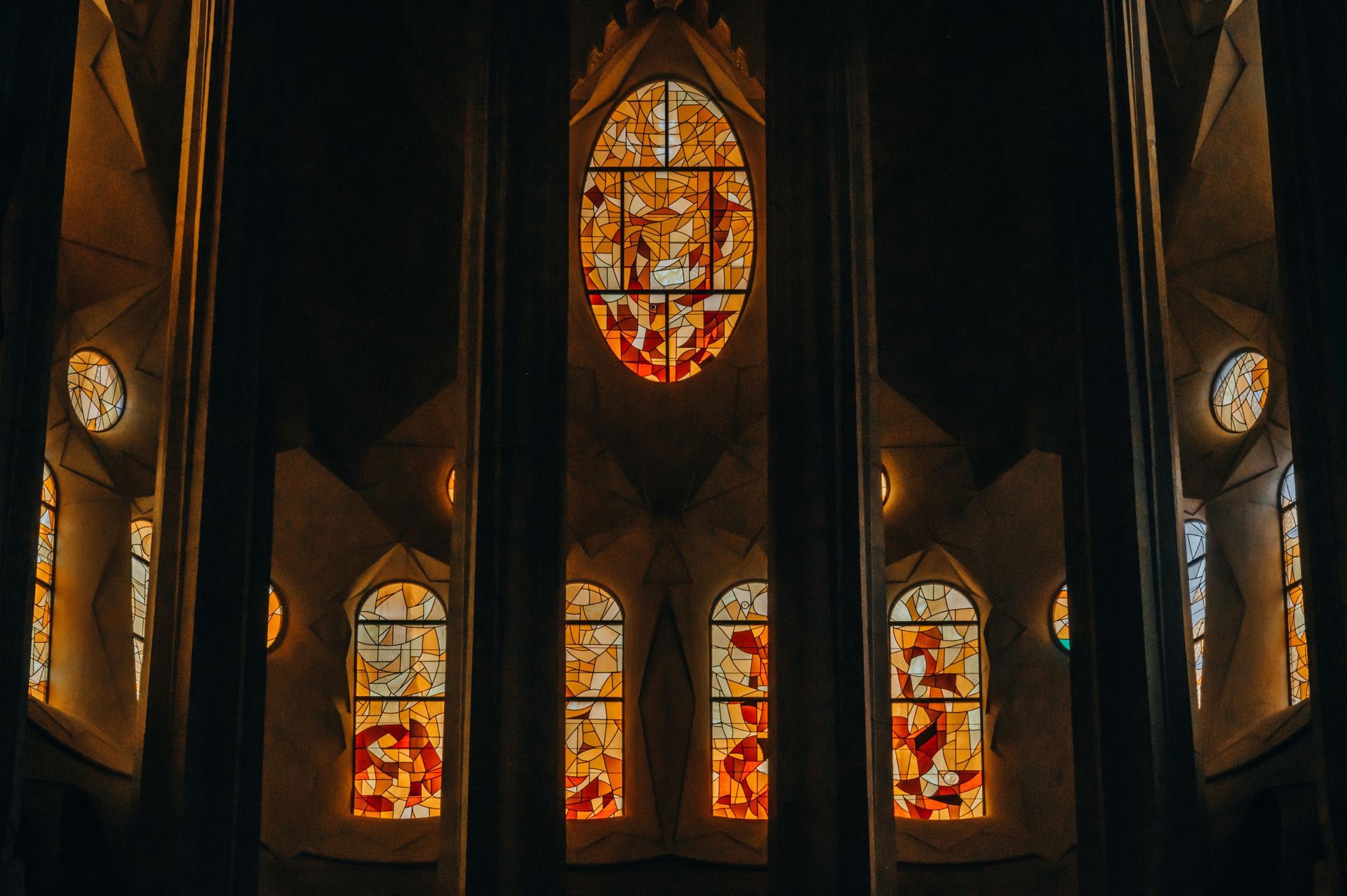 Stained glass windows within a cathedral, illuminated by warm sunlight, creating an orange and yellow glow.