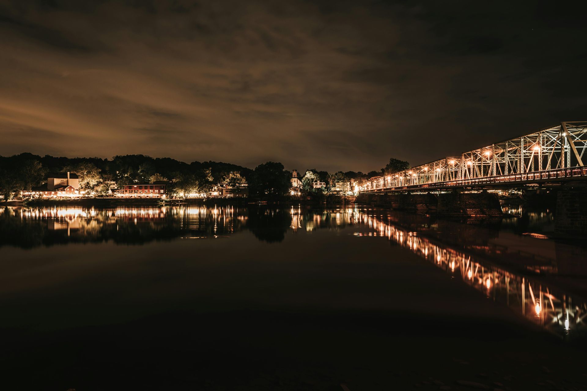 Norwich. Night view of a lit bridge over still water, reflecting the lights of the structure and nearby buildings.