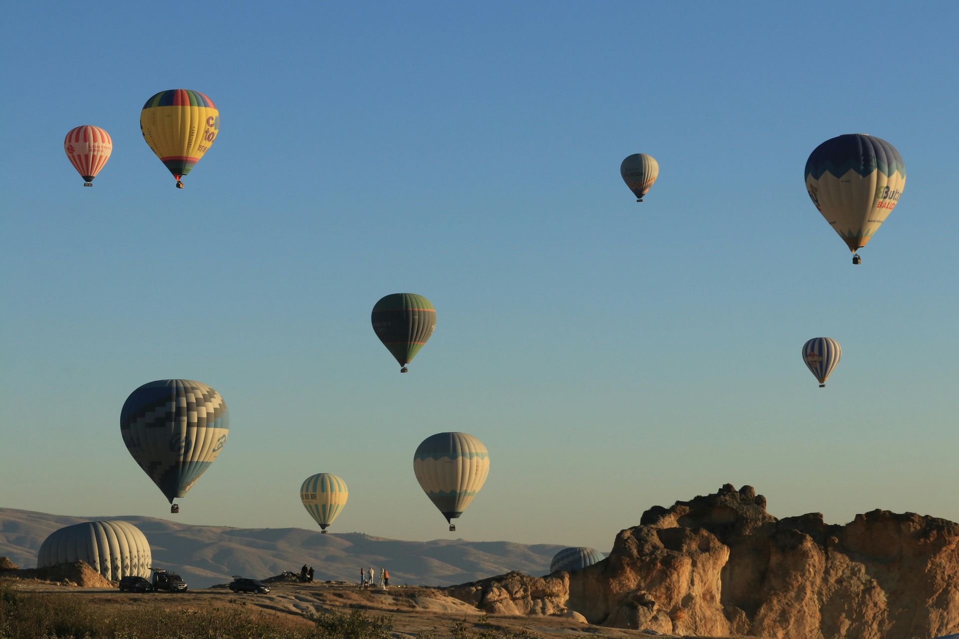 Hot air balloons drift over a rocky landscape under a blue sky.