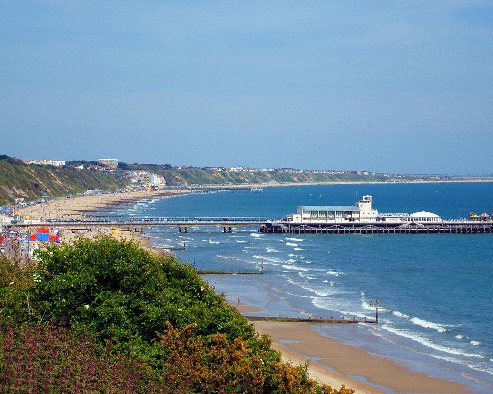 Bournemouth. Ocean view with a pier extending into the water, sandy beach, buildings on the coast, clear blue sky.