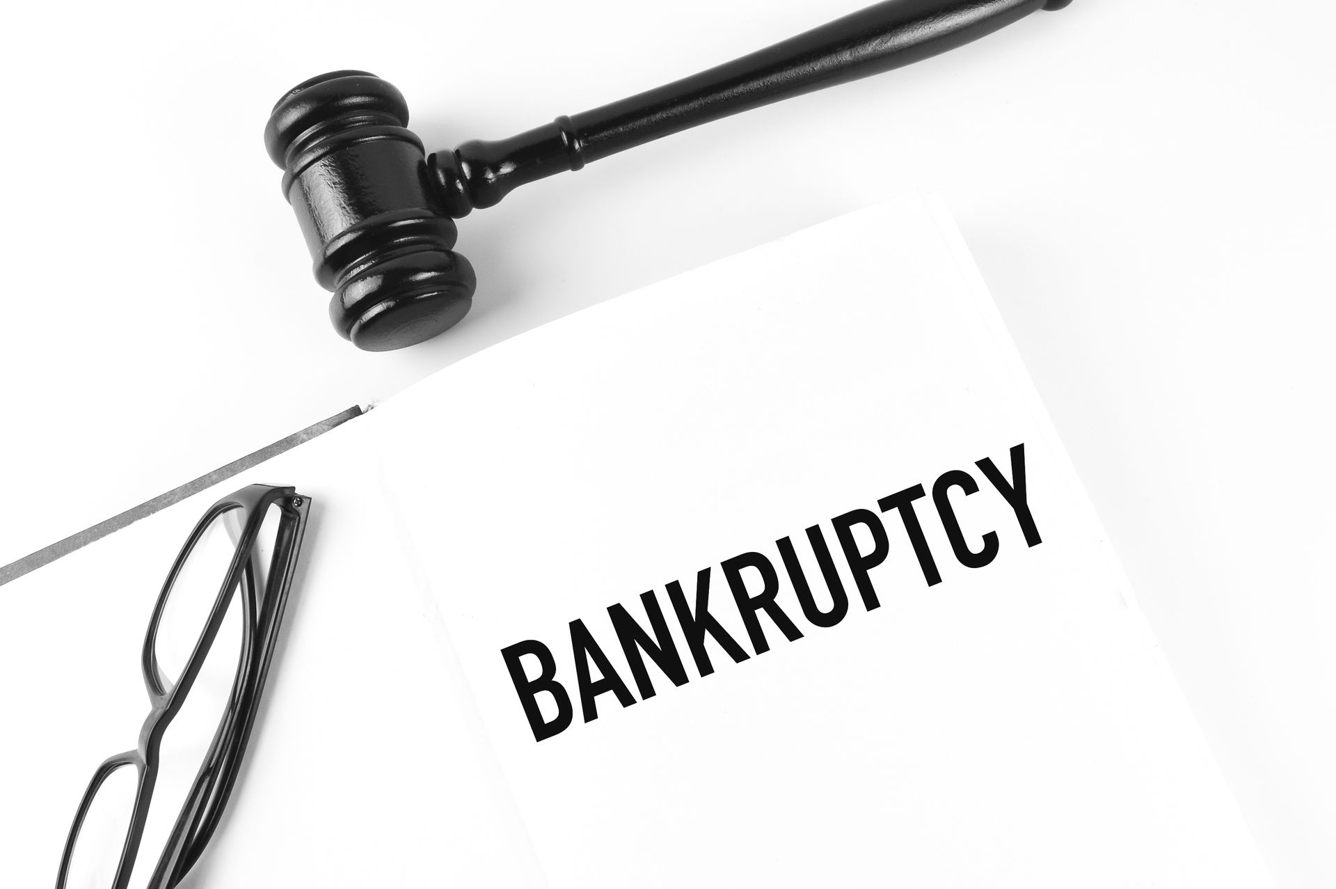 Close-up of a judge's gavel, a pair of glasses, and a bankruptcy document on a white background.