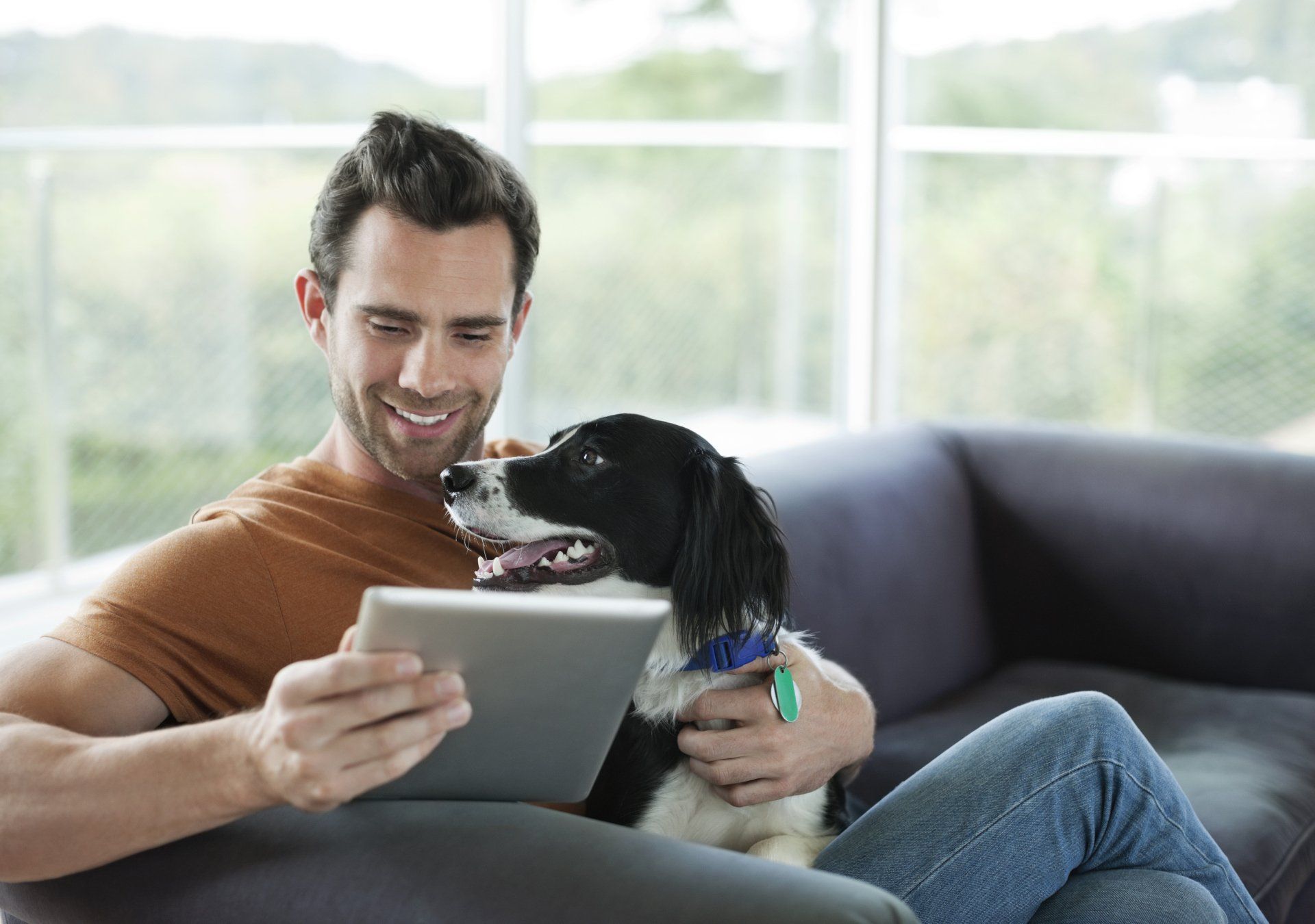 man checking a tablet with a dog on his lap