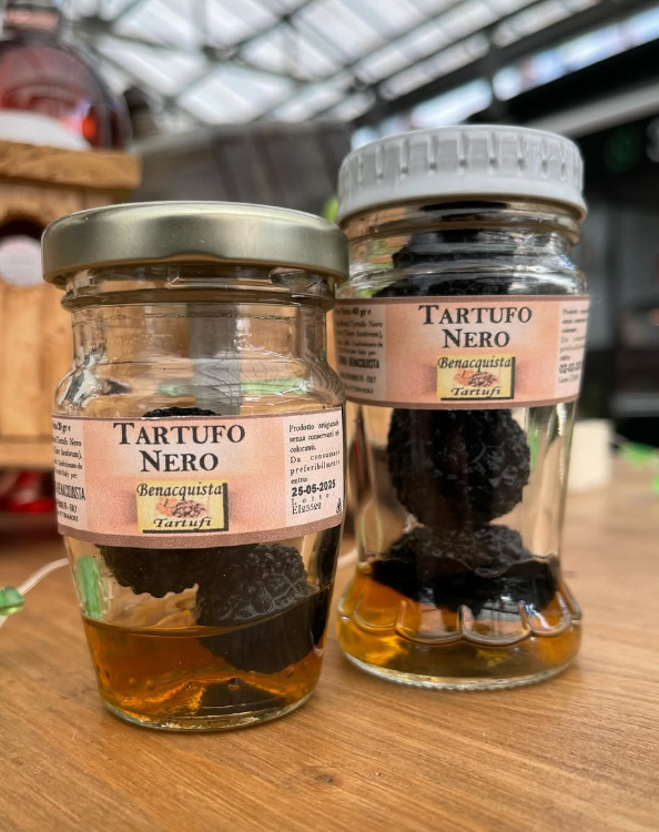 Due barattoli di tartufo nero sono appoggiati su un tavolo di legno.