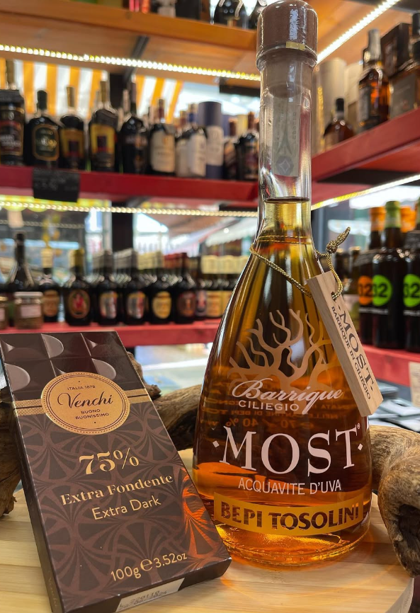 Una bottiglia di mosto è appoggiata su un tagliere di legno accanto a una scatola di cioccolatini.