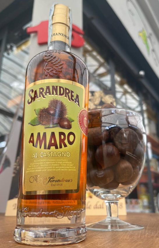 Una bottiglia di amaro accanto a un bicchiere di castagne ricoperte di cioccolato.