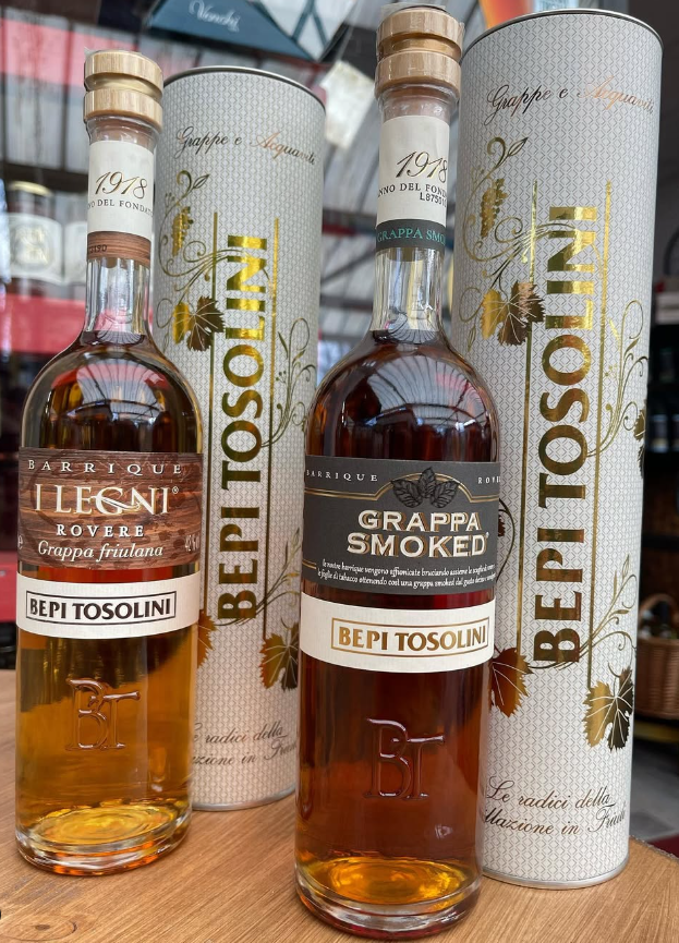 Tre bottiglie di grappa affumicata sono appoggiate su un tavolo di legno.