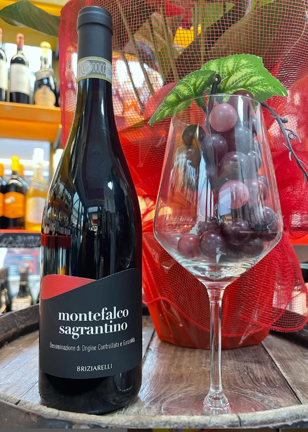 Una bottiglia di vino è accanto a un bicchiere di vino pieno d'uva.