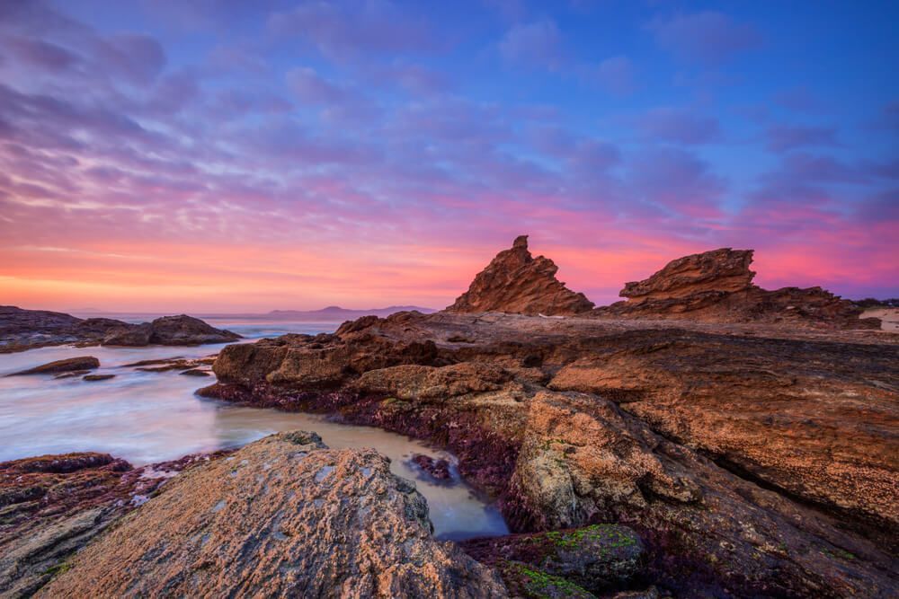 A Sunset Over A Rocky Beach With A Large Rock In The Foreground — Coffs Coast Building Pty Ltd in Nambucca Heads, NSW