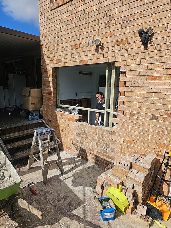 A Man Is Working On A Window In A Brick Building — Coffs Coast Building Pty Ltd in Toormina, NSW