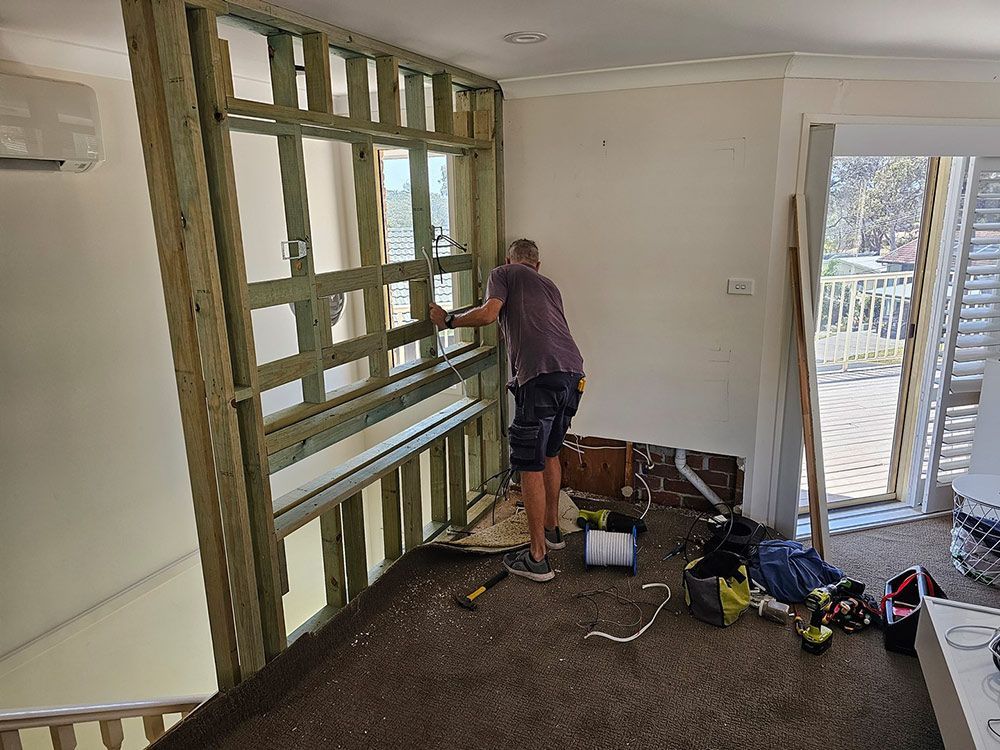 A Man Is Working On A Wall In A Living Room — Coffs Coast Building Pty Ltd in Toormina, NSW