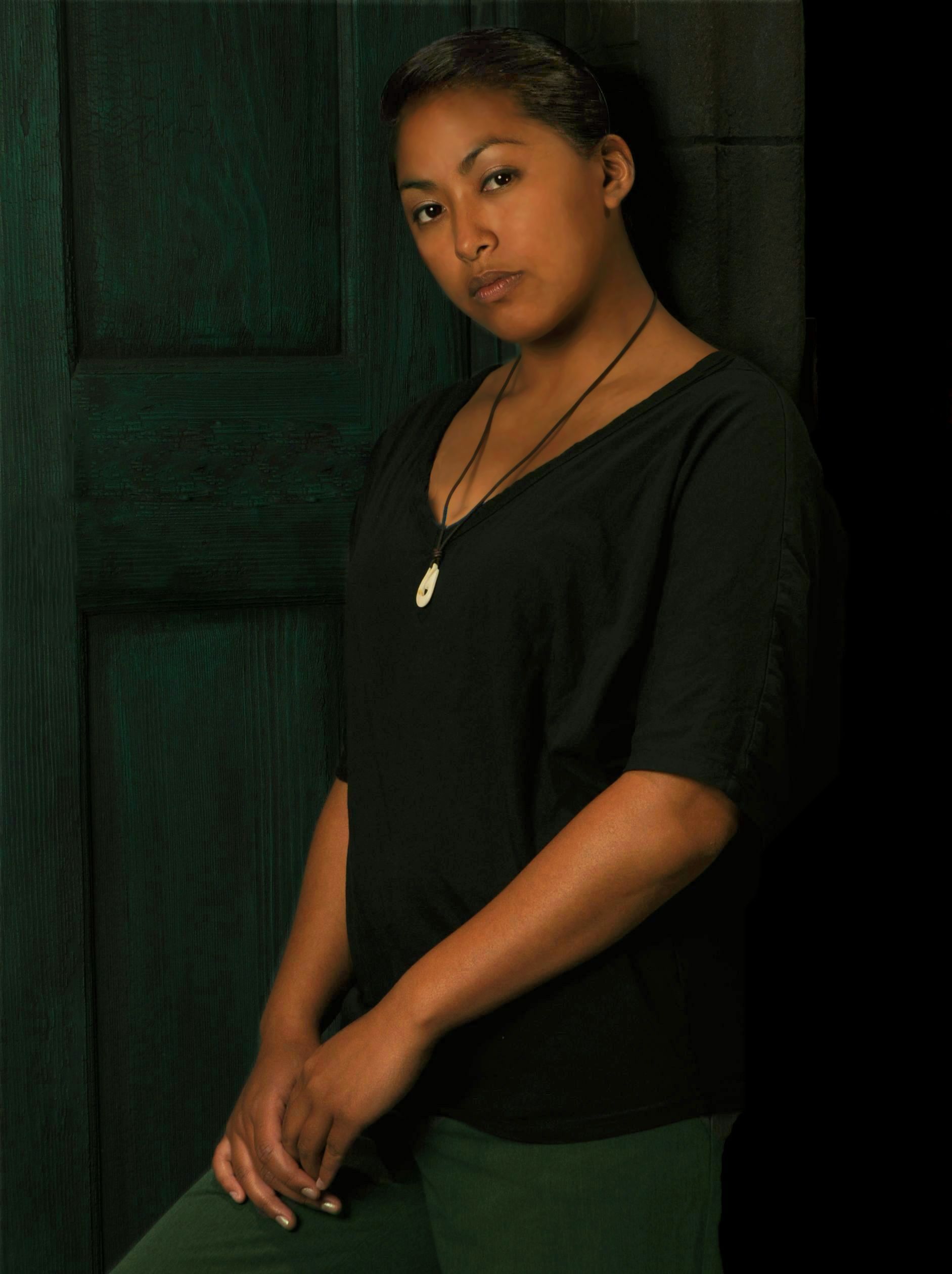 a woman wearing a black shirt and green pants is leaning against a wall