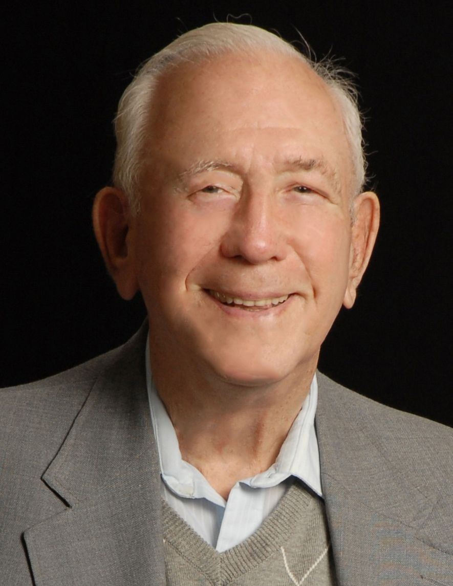 a man in a suit and sweater smiles for the camera