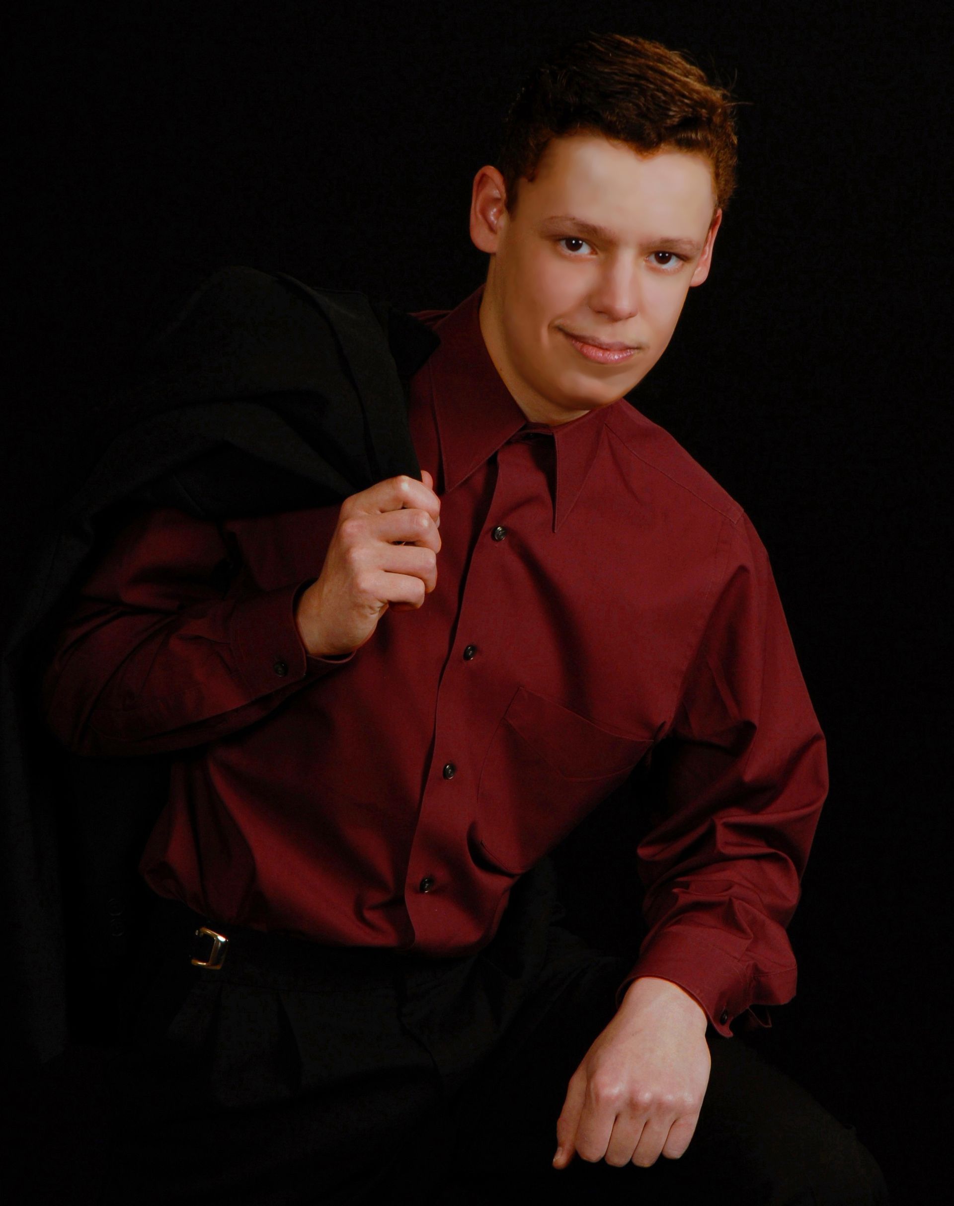 a young man in a red shirt is holding a black jacket over his shoulder