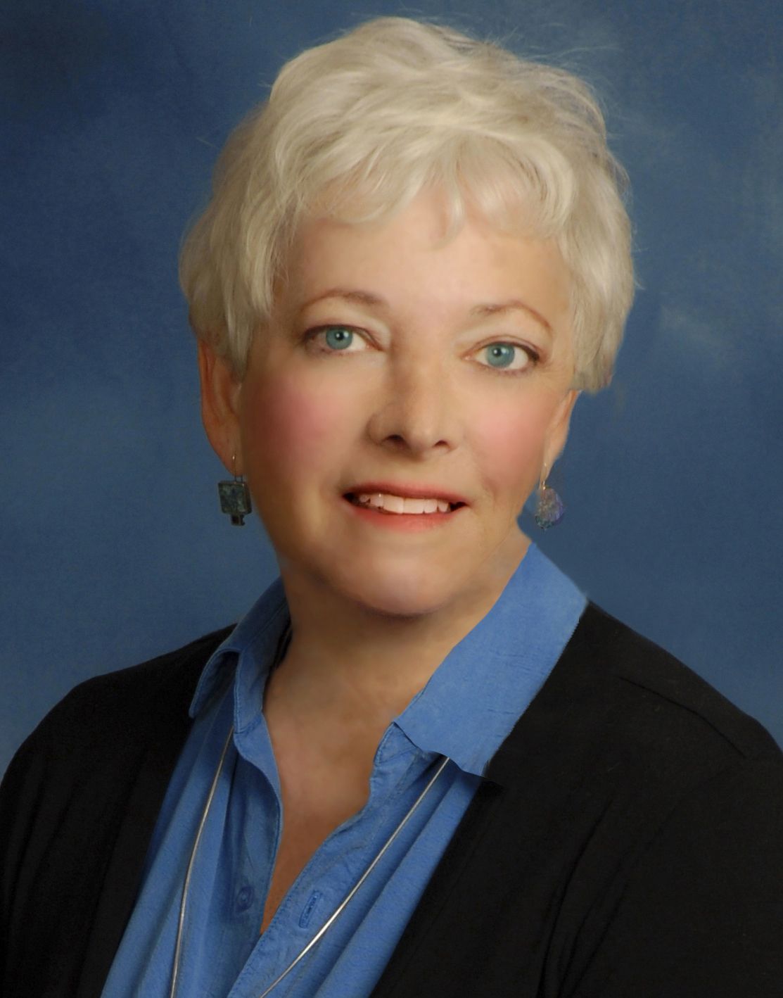 a woman in a blue shirt and black sweater smiles for the camera