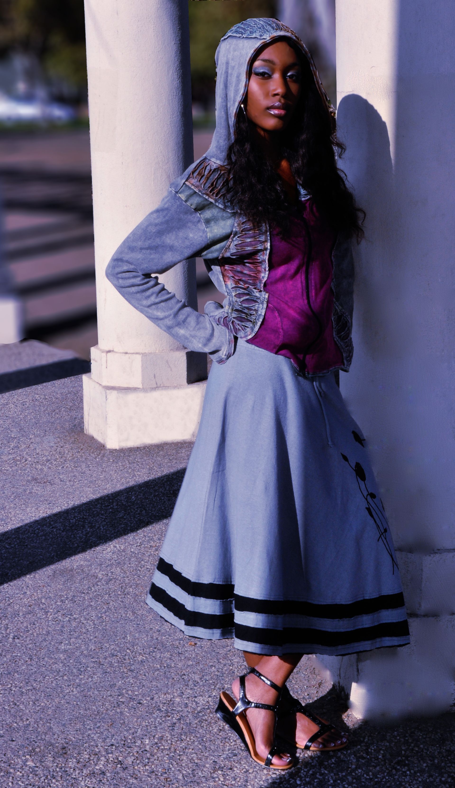 a woman wearing a hooded jacket and a skirt is leaning against a wall