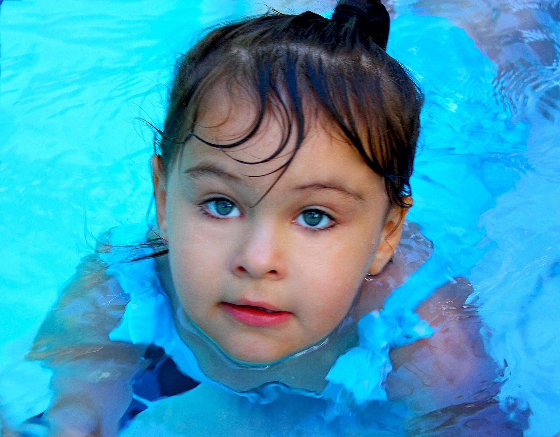 a little girl is swimming in a pool and looking at the camera .