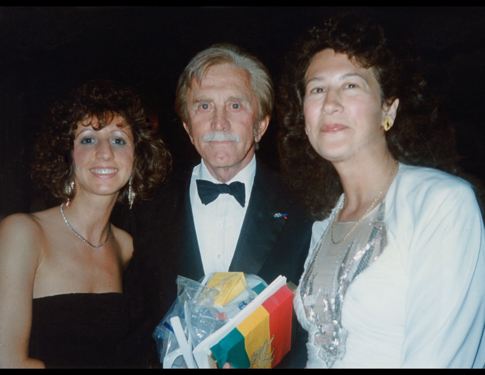 a man in a tuxedo poses with two women