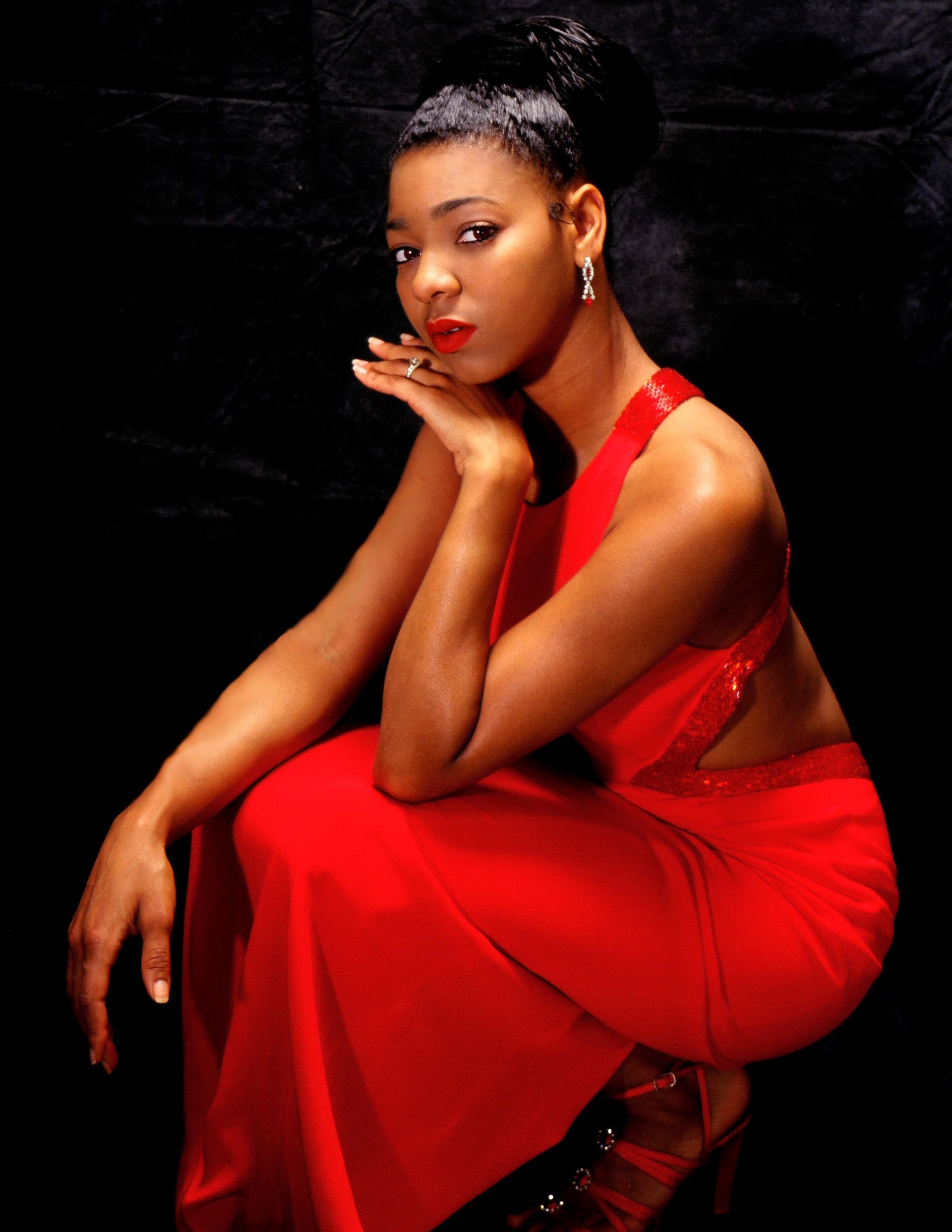 a woman in a red dress sits with her hand on her chin