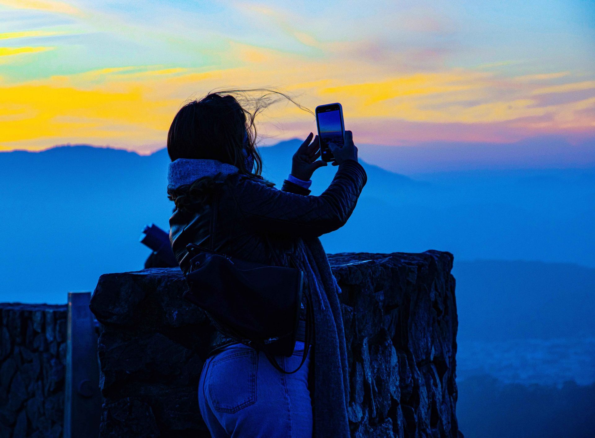 a woman is taking a picture of the sunset with her cell phone .