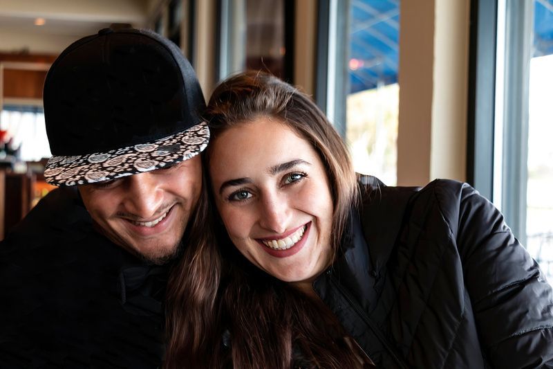 a man and a woman are smiling for the camera while sitting next to each other in front of a window .