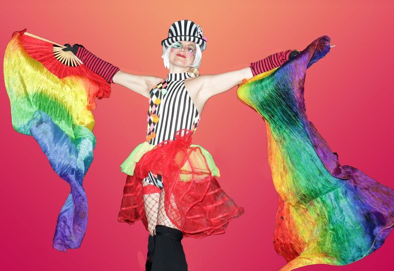 a woman in a clown costume is holding a rainbow fan .