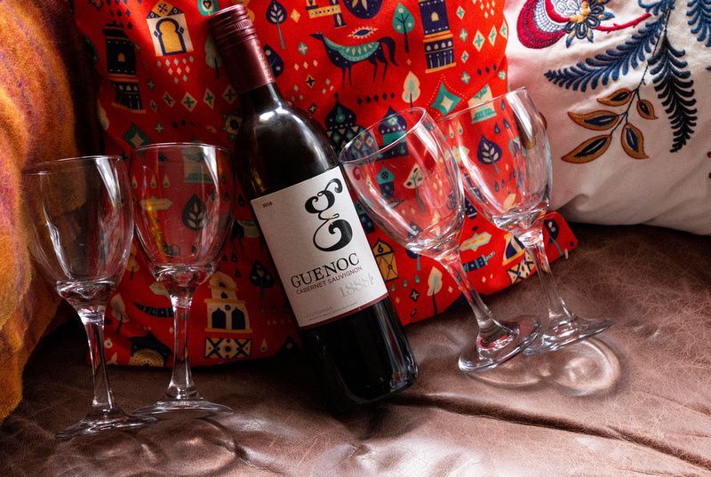 a bottle of wine is sitting on a bed next to three wine glasses .